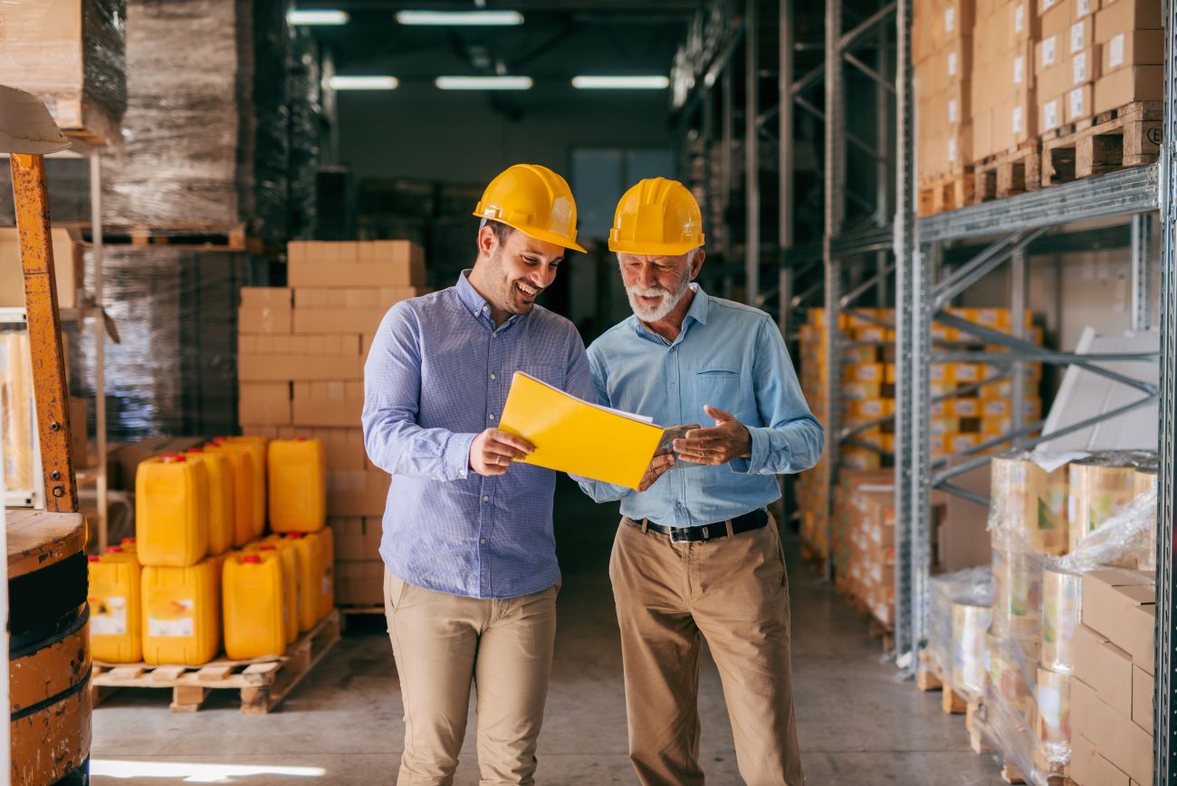Two men in hard hats stand together in a spacious warehouse.