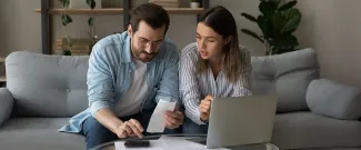 A couple sitting on a couch working on a laptop together.